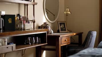 A bedroom with a bed, a desk with a lamp, a mirror, and a shelf with various items.