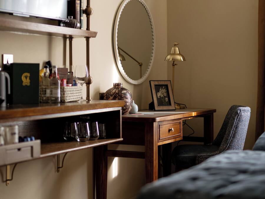 A bedroom with a bed, a desk with a lamp, a mirror, and a shelf with various items.