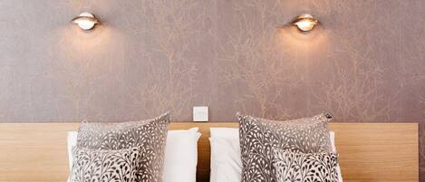 A neatly made bed with patterned pillows, a wooden headboard, and two wall-mounted lights.