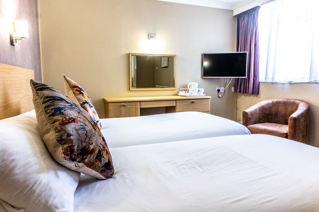A hotel room with two beds, a desk with a flat-screen TV, a chair, and a window with curtains.