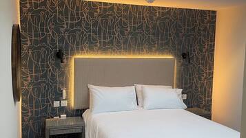 A modern hotel room with a skylight, a patterned wall, a large bed, and a nightstand with a lamp.