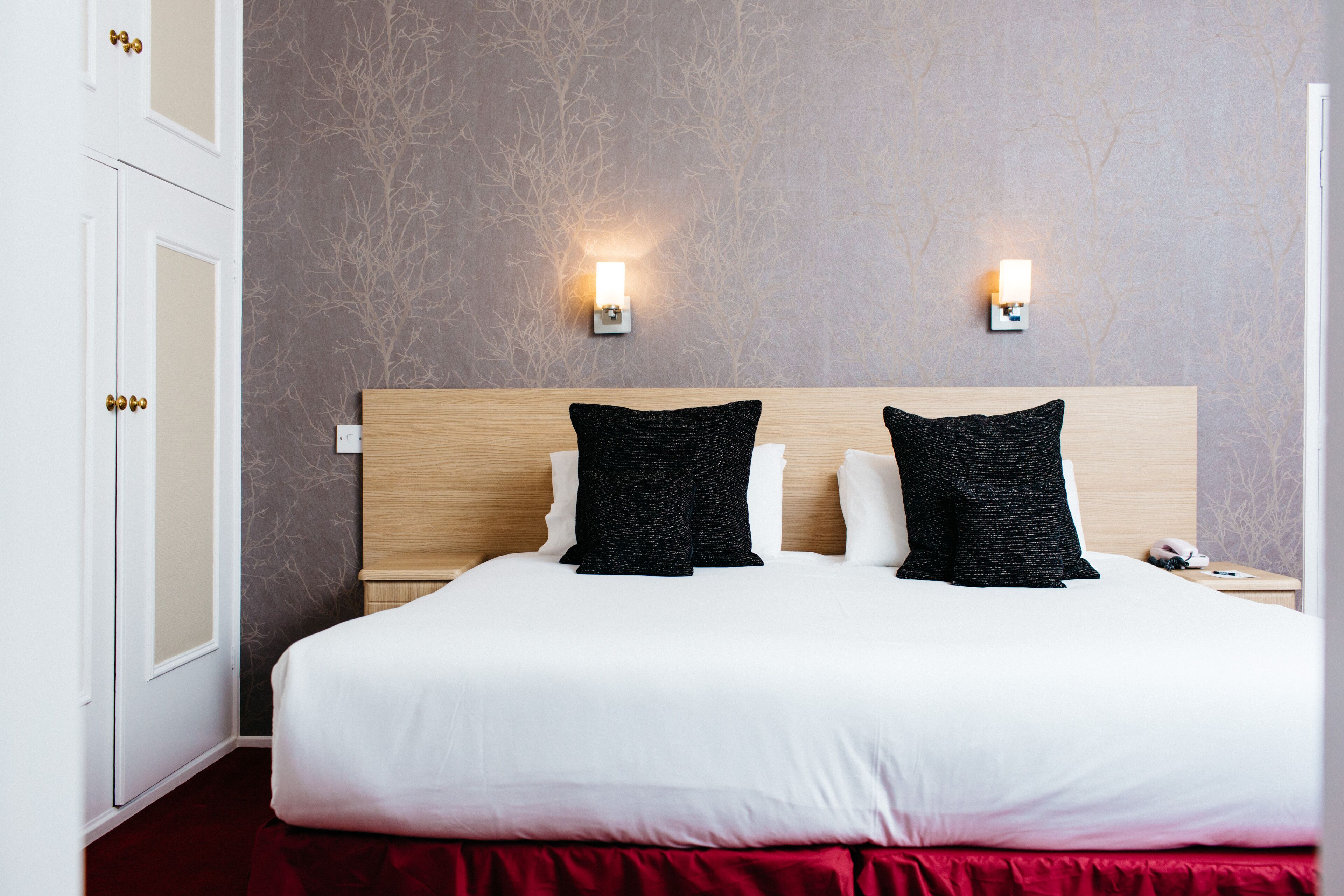 Une chambre d’hôtel avec un grand lit, deux lampes de chevet, une tête de lit en bois et un mur d’accent rouge.