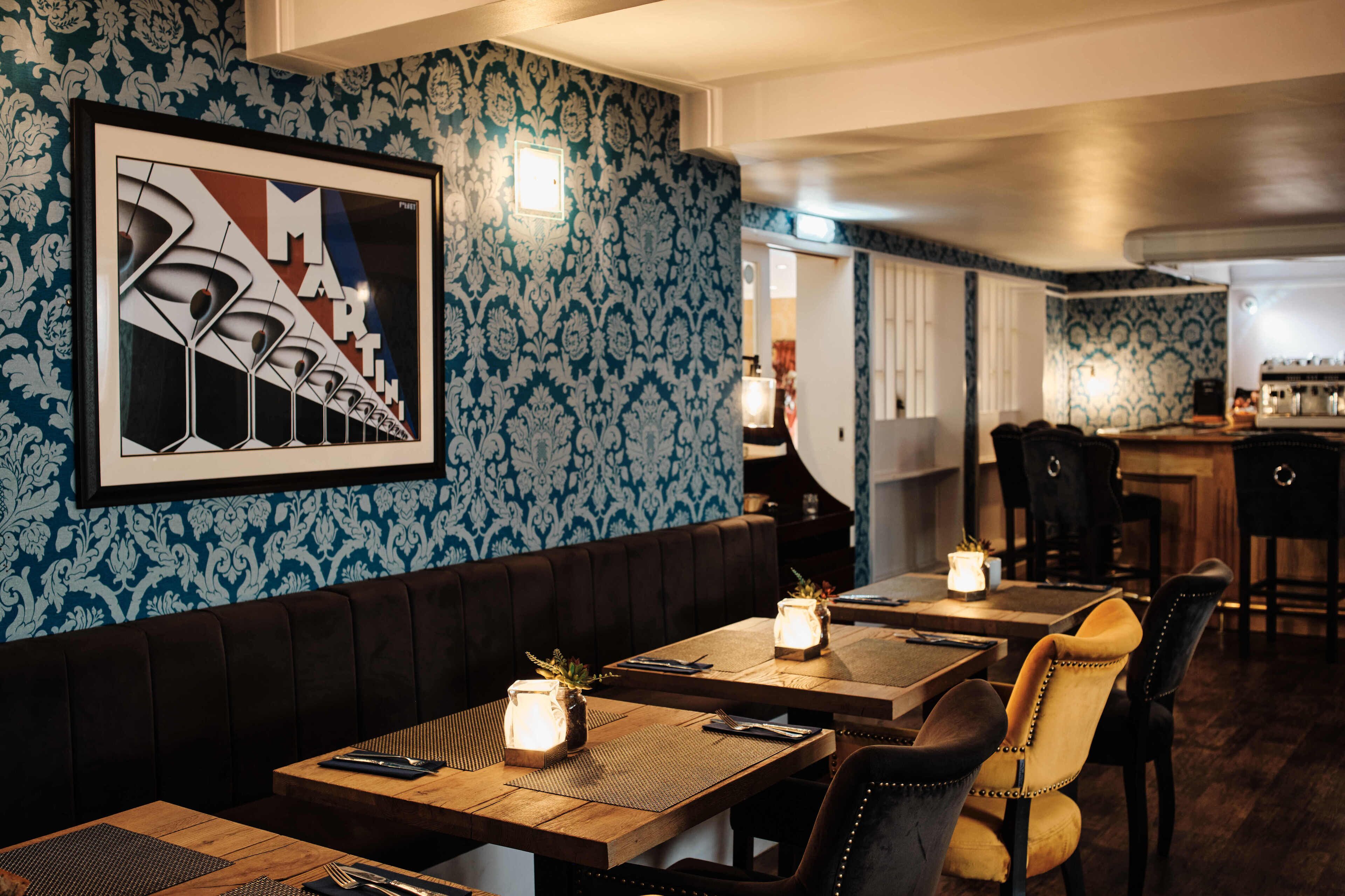 Un restaurant avec des tables en bois, des banquettes confortables et un papier peint à motifs.
