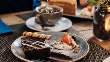 Une personne verse du thé dans une tasse, une assiette avec une part de gâteau, et un petit pot contenant une plante, le tout sur une table.