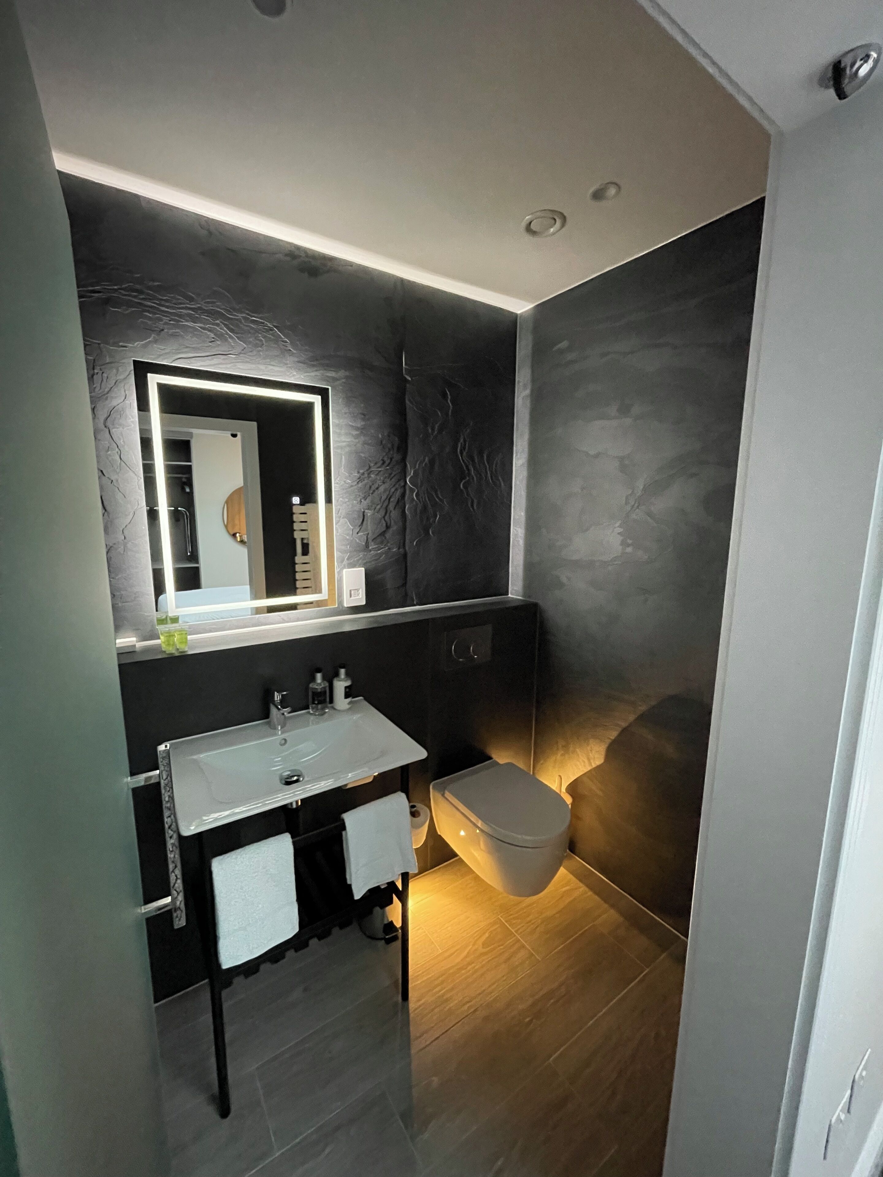 A modern bathroom with a dark wall, a white sink, a mirror, and a toilet.