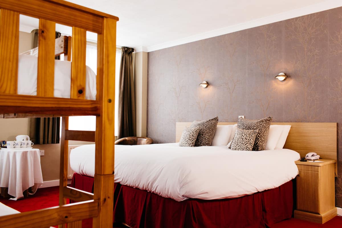 Una habitación de hotel con una cama litera, una mesita de noche con lámpara y una alfombra roja.