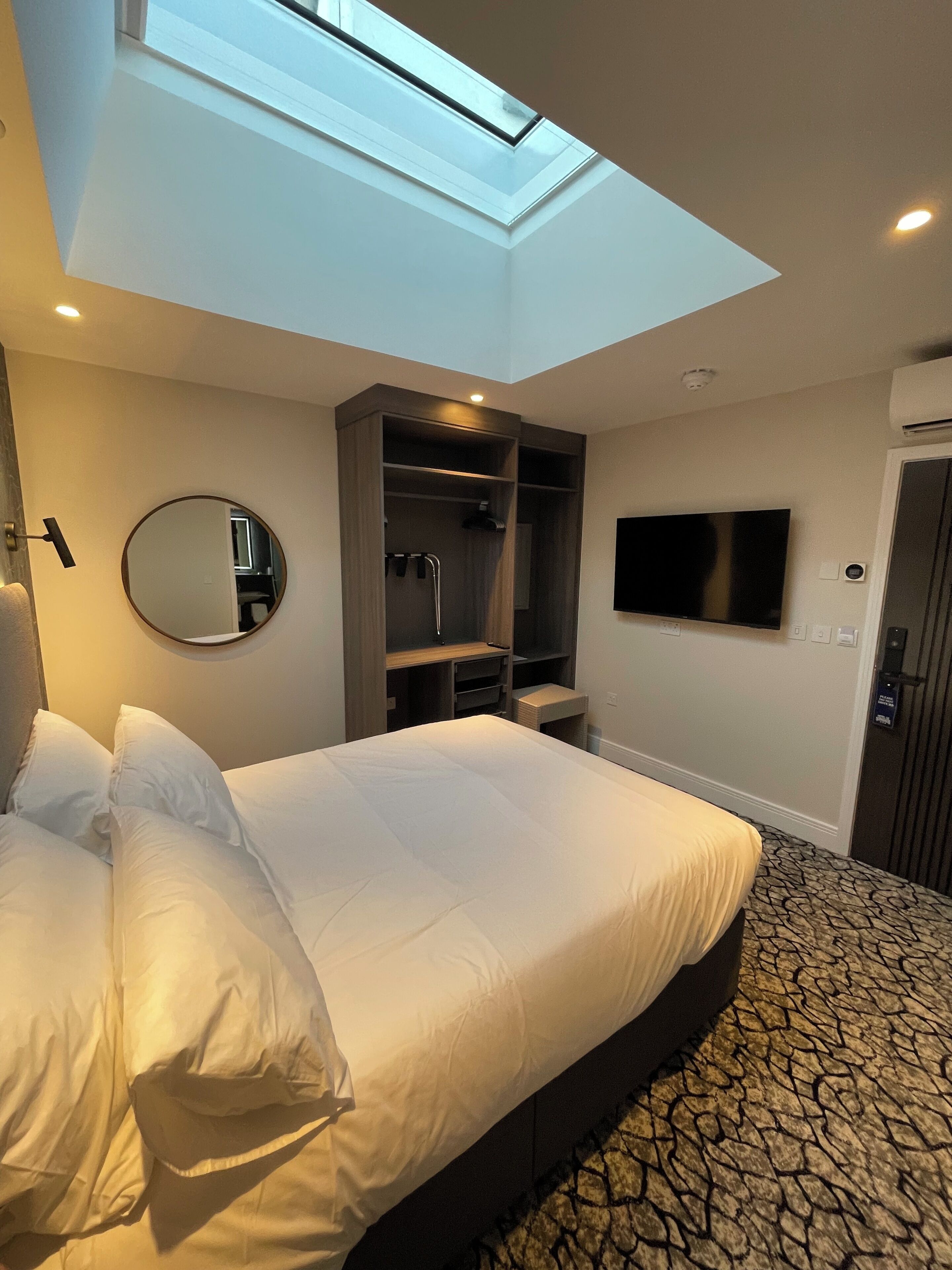 Habitación de hotel con una cama grande, tragaluz, vestidor, televisor y alfombra estampada.