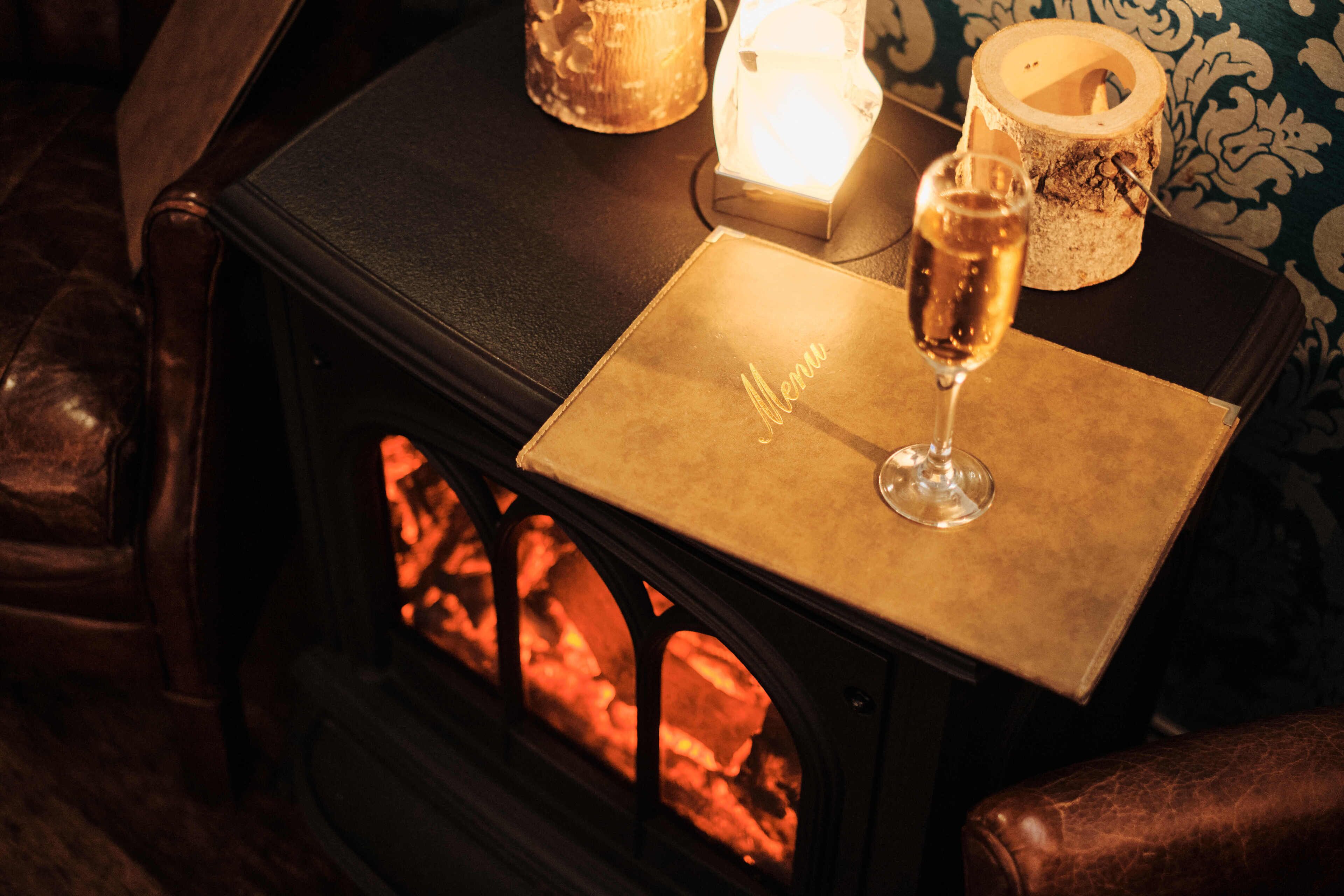 A cozy room with a wood-burning stove, a glass of champagne, and a menu on the table.