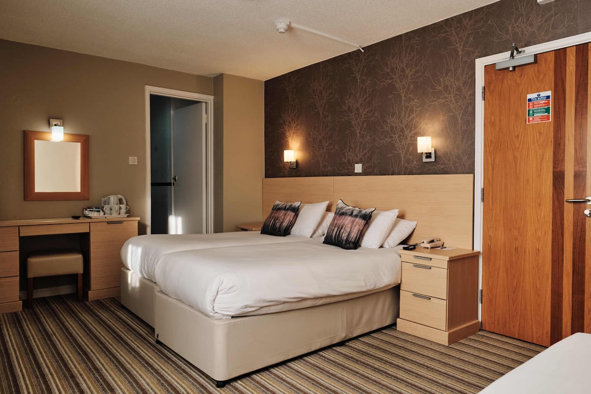 Una habitación de hotel con una cama grande, un escritorio con una silla, una mesita de noche y un armario.