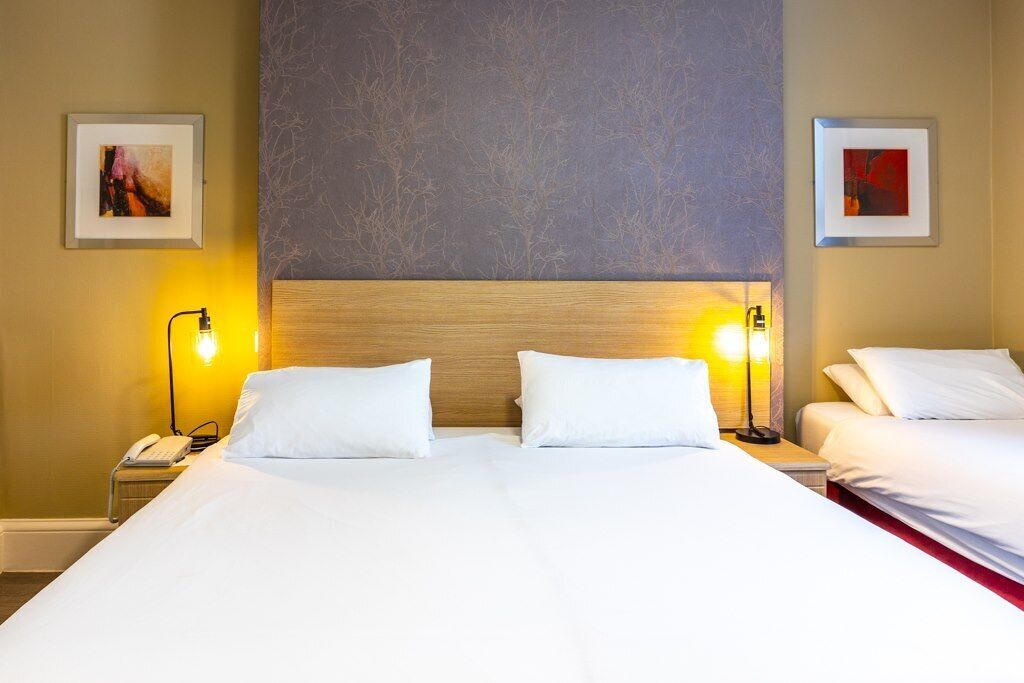 A hotel room with a large bed, two bedside lamps, and two framed pictures on the walls.