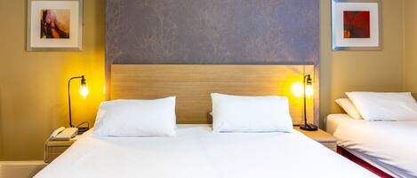A hotel room with a large bed, two bedside lamps, and two framed pictures on the walls.