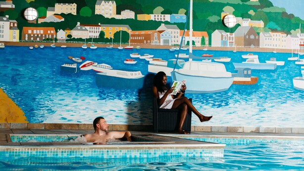 Zona de piscina con un mural que muestra barcos y edificios al fondo.