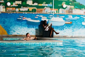 Zona de piscina con un mural que muestra barcos y edificios al fondo.