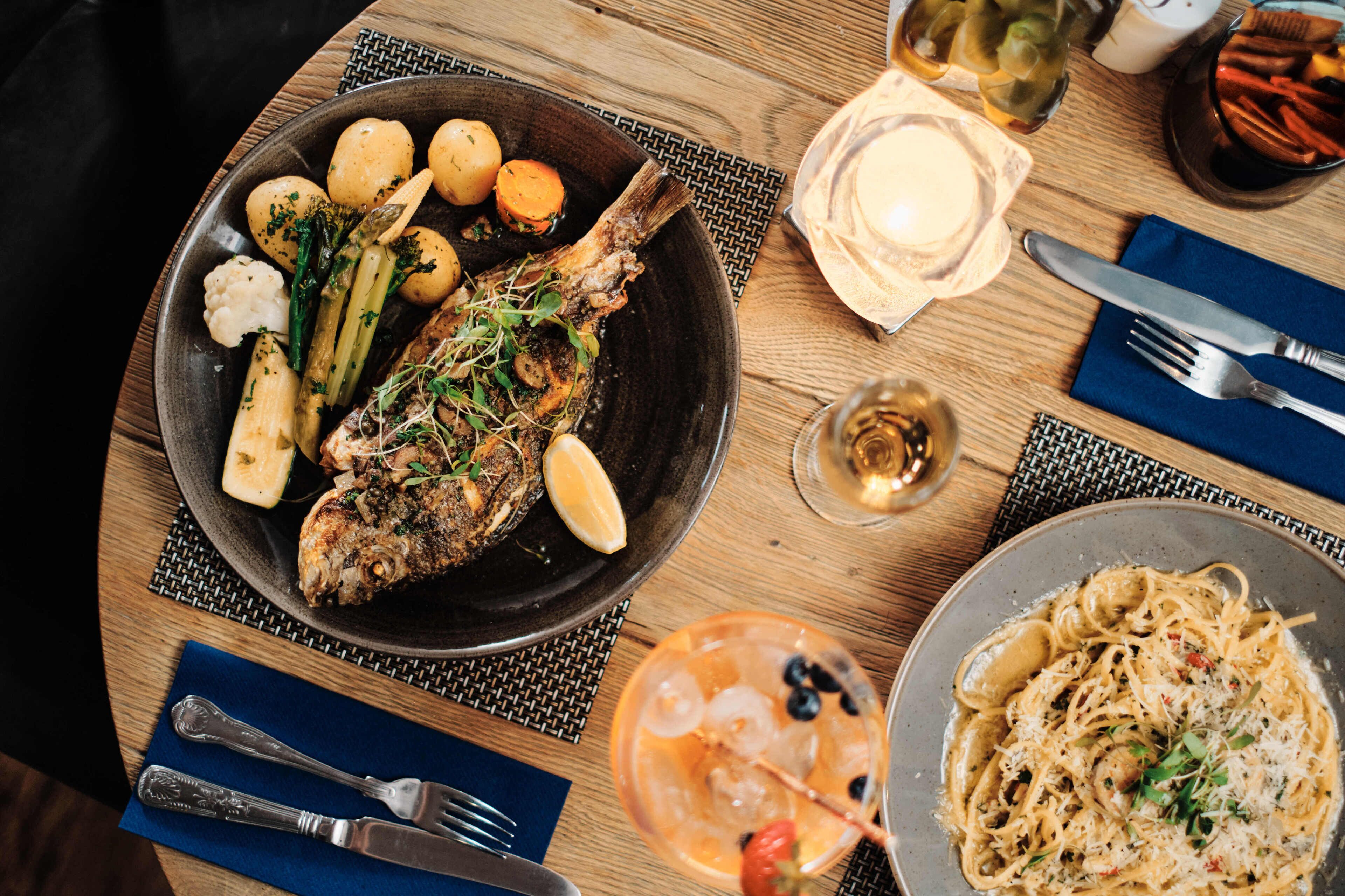 A dining table with a plate of fish, vegetables, and a glass of drink.