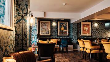 A restaurant interior with patterned wallpaper, framed artwork, and leather seating.