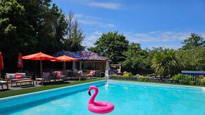 A swimming pool with a pink flamingo float, surrounded by lounge chairs and umbrellas. - Le Pommier (Castel)