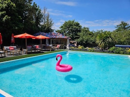 Una piscina con un flotador con forma de flamenco rosa, rodeada de sillas de descanso y sombrillas.