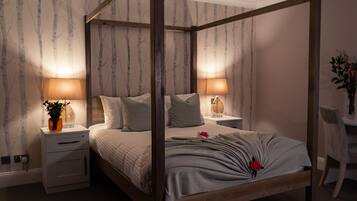 A four-poster bed with a wooden frame, two bedside tables with lamps, a nightstand, and a chair.
