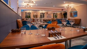 A dining area with a long wooden table set for a meal, surrounded by blue and orange chairs. - Le Pommier (Castel)