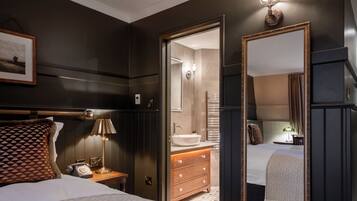 A hotel room with a bed, bedside table, lamp, dresser, mirror, and a bathroom visible through an open door.