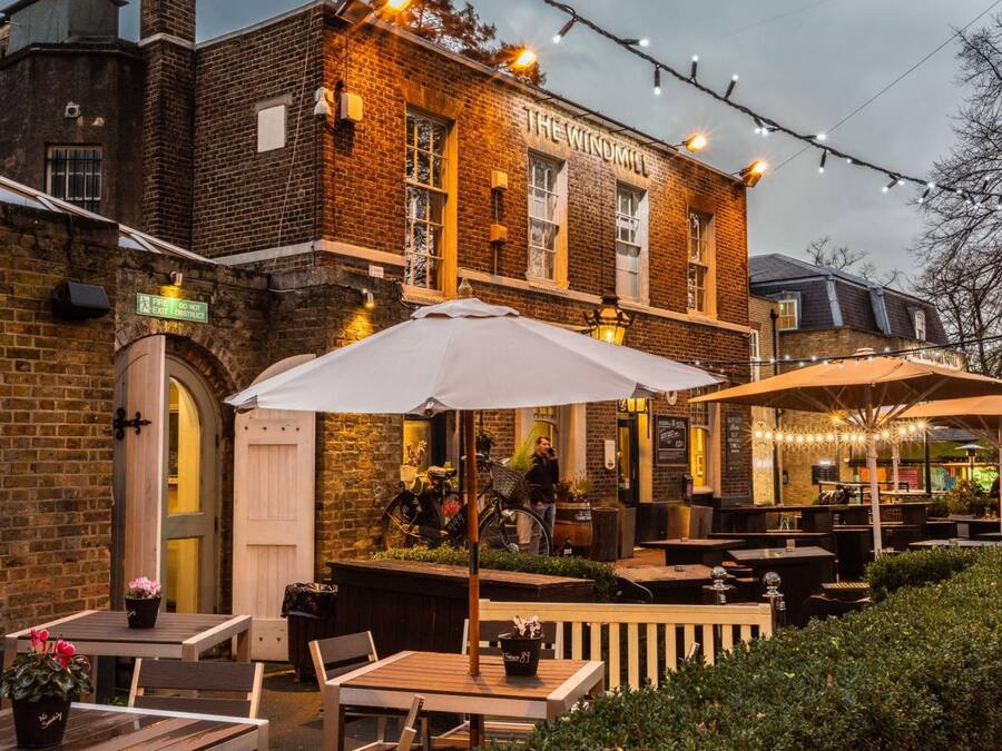 An outdoor seating area with tables and umbrellas at The Windmill pub.