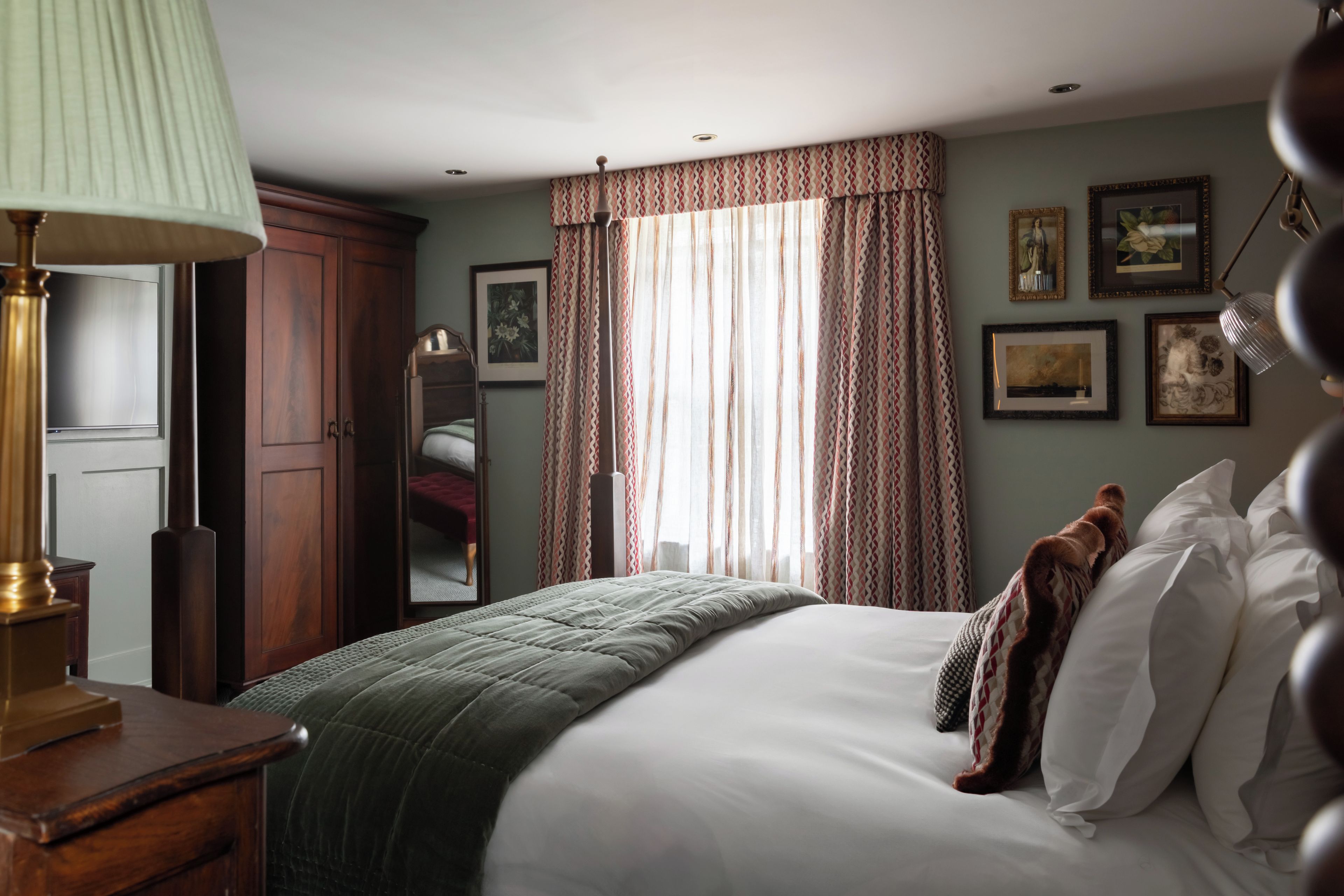 A bedroom with a bed, a dresser, a mirror, and a window with curtains.