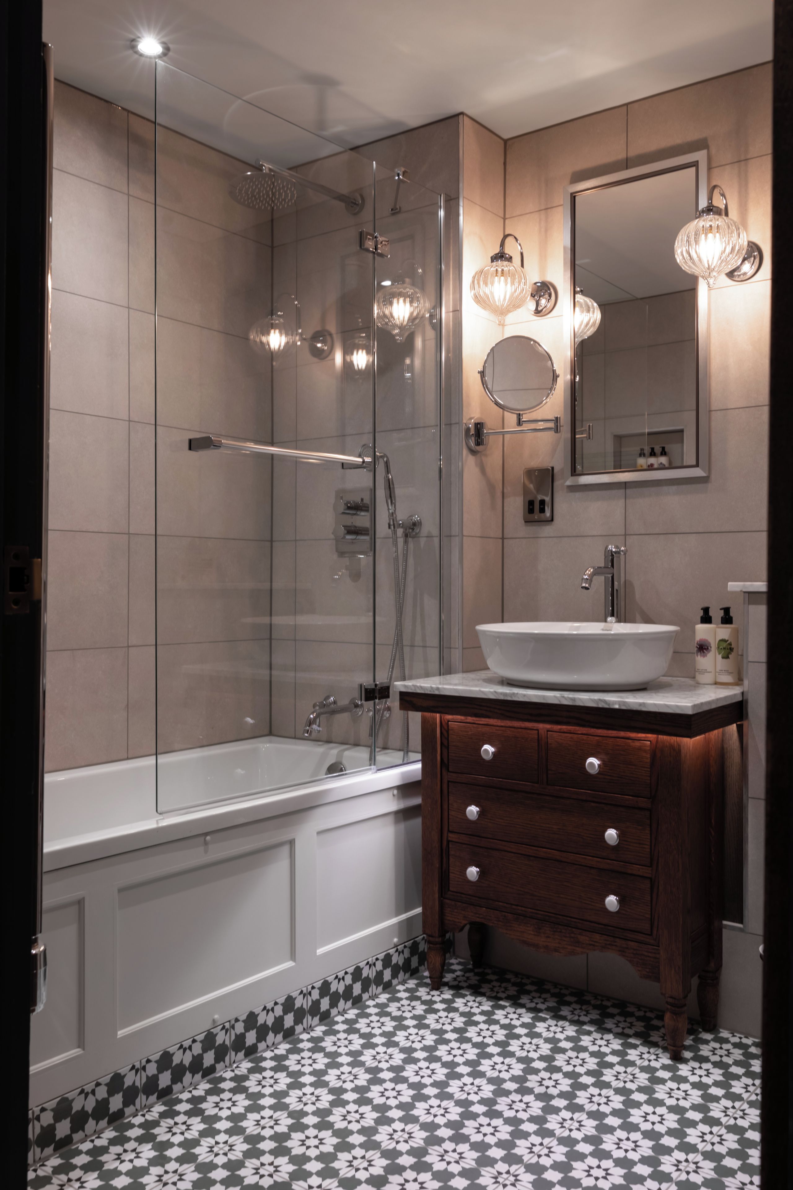 Un baño moderno con ducha de vidrio, bañera blanca, tocador de madera con lavamanos y espejo sobre el tocador.
