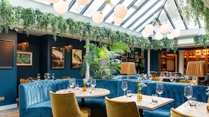 Un restaurante con cabinas de terciopelo azul, sillas amarillas y un jardín en el techo.