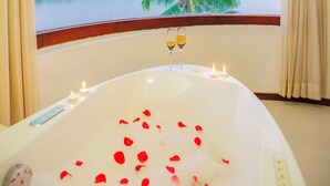 Una bañera con pétalos de rosa y velas, vista a un lago y una palmera.