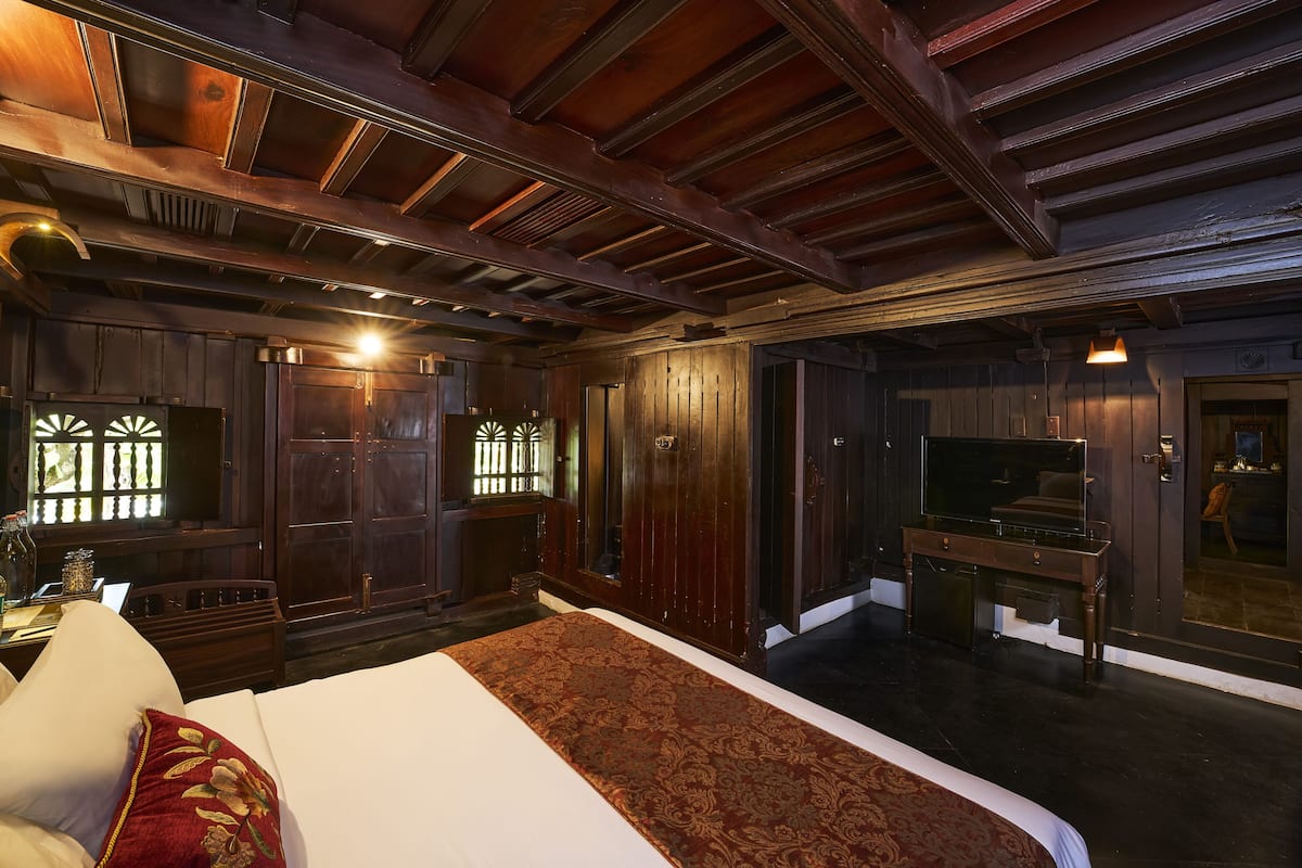 A spacious bedroom with a large bed, wooden ceiling beams, and a television.