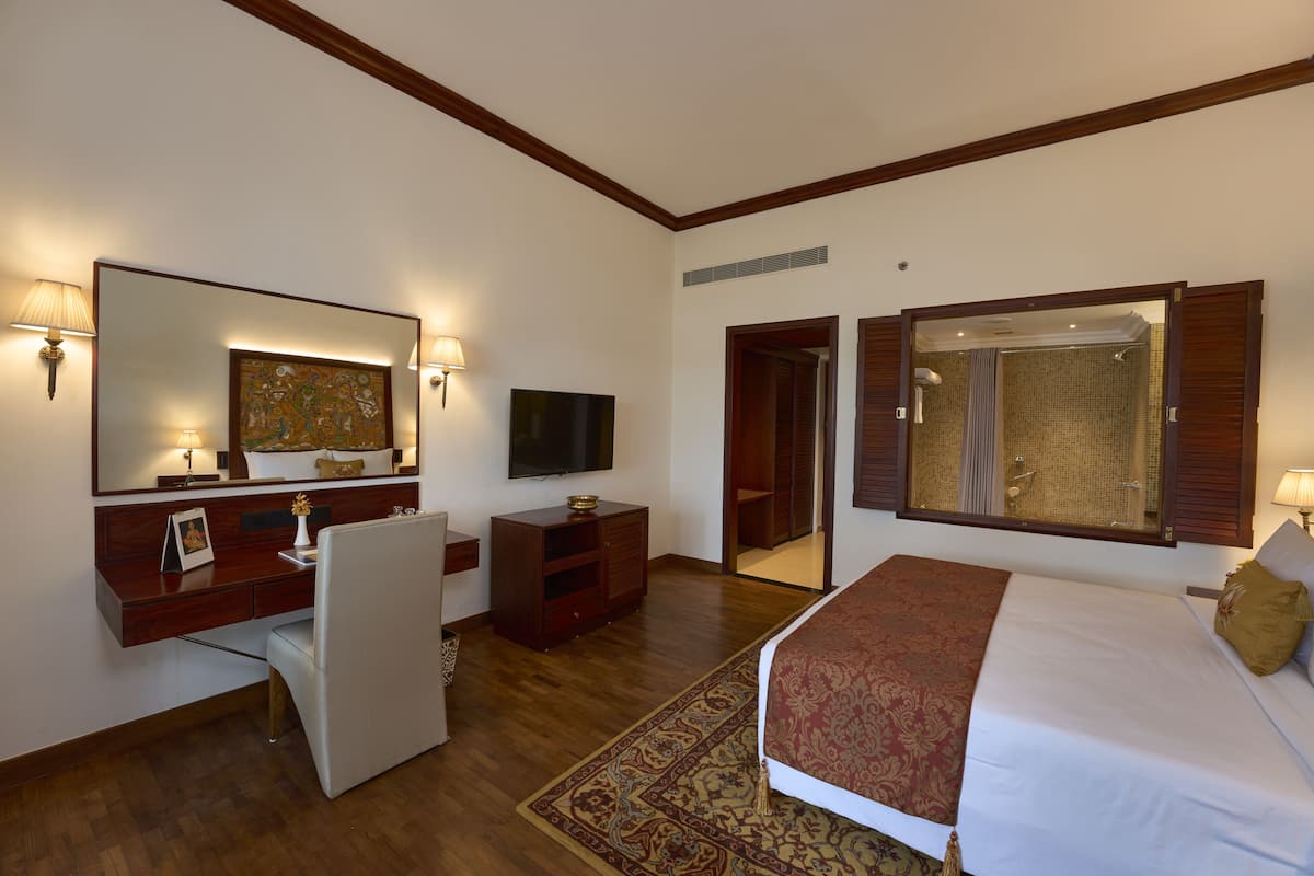 A hotel room with a bed, a desk with a chair, a television, a wardrobe, and a bathroom with a shower and toilet.