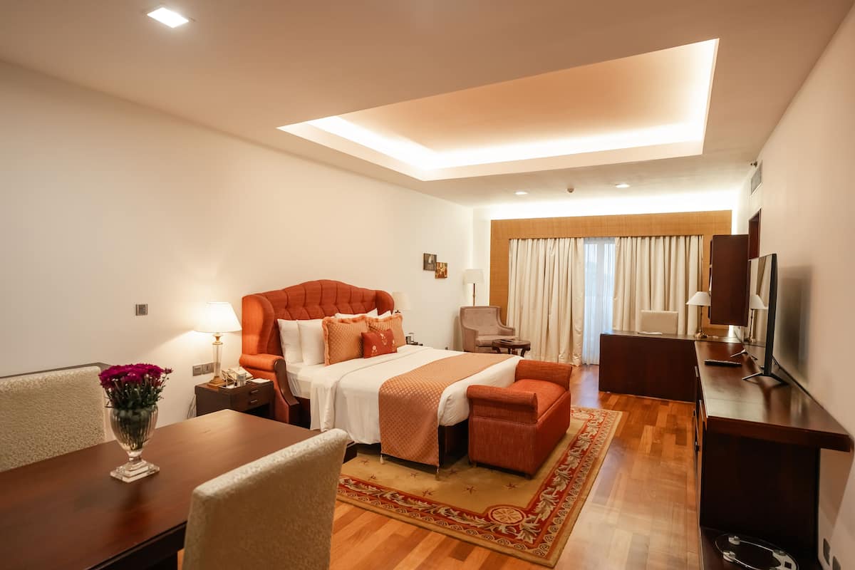 A modern hotel room with a large bed, a desk, a chair, a TV, and a ceiling light.