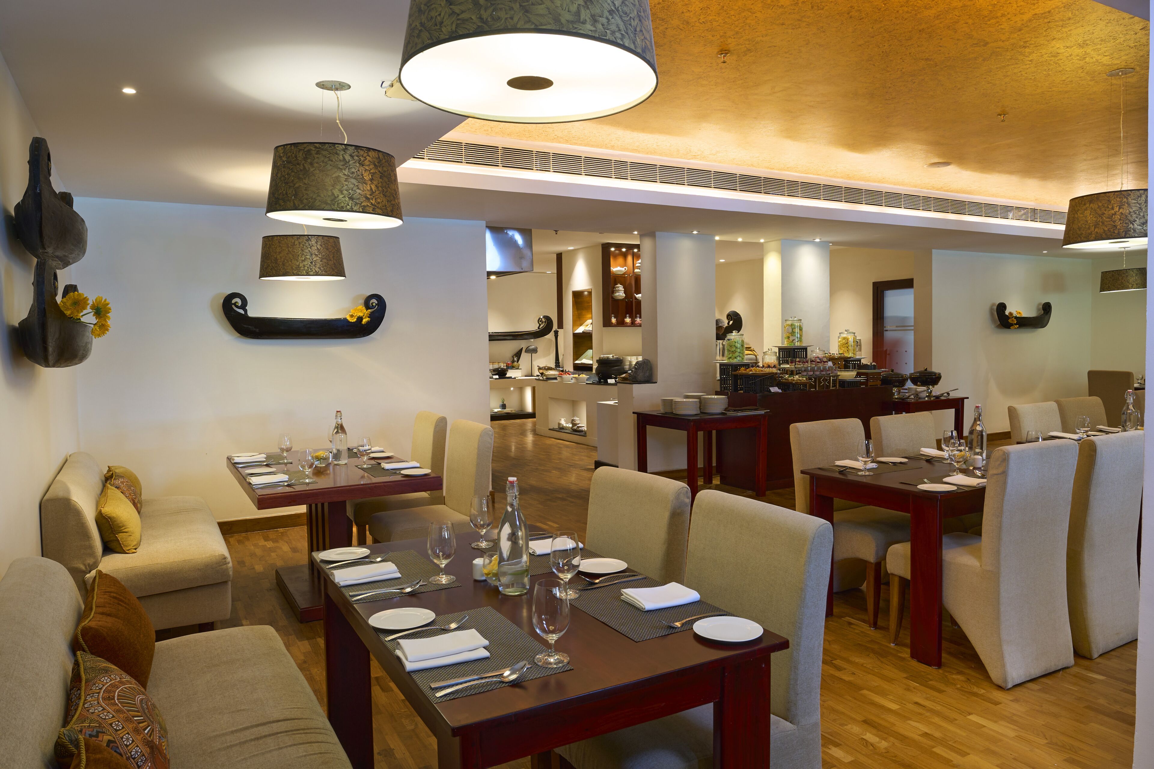 A dining area with multiple tables set for meals, a kitchen in the background, and a modern interior design.