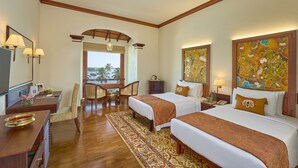A hotel room with two beds, a desk, a chair, a TV, and artwork on the walls.