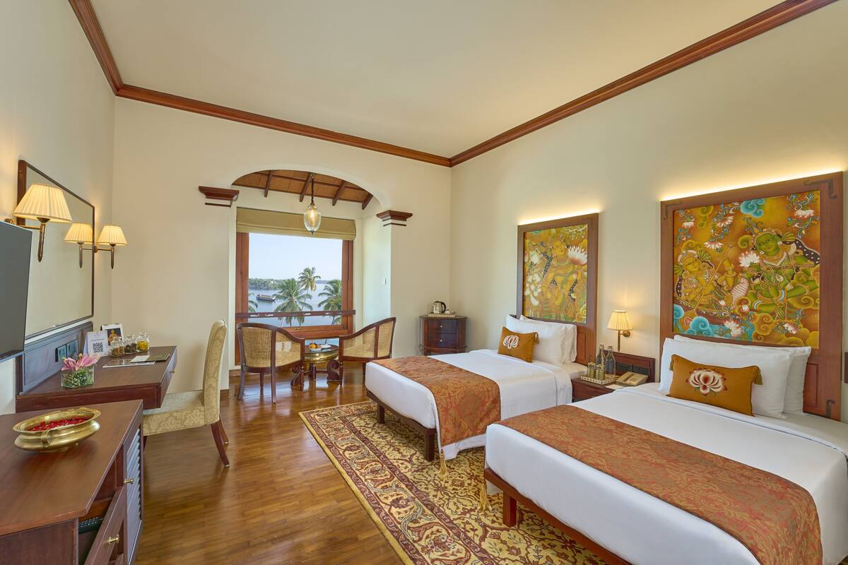 A hotel room with two beds, a desk, a chair, a TV, and artwork on the walls.