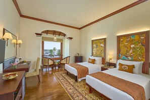 A hotel room with two beds, a desk, a chair, a TV, and artwork on the walls.