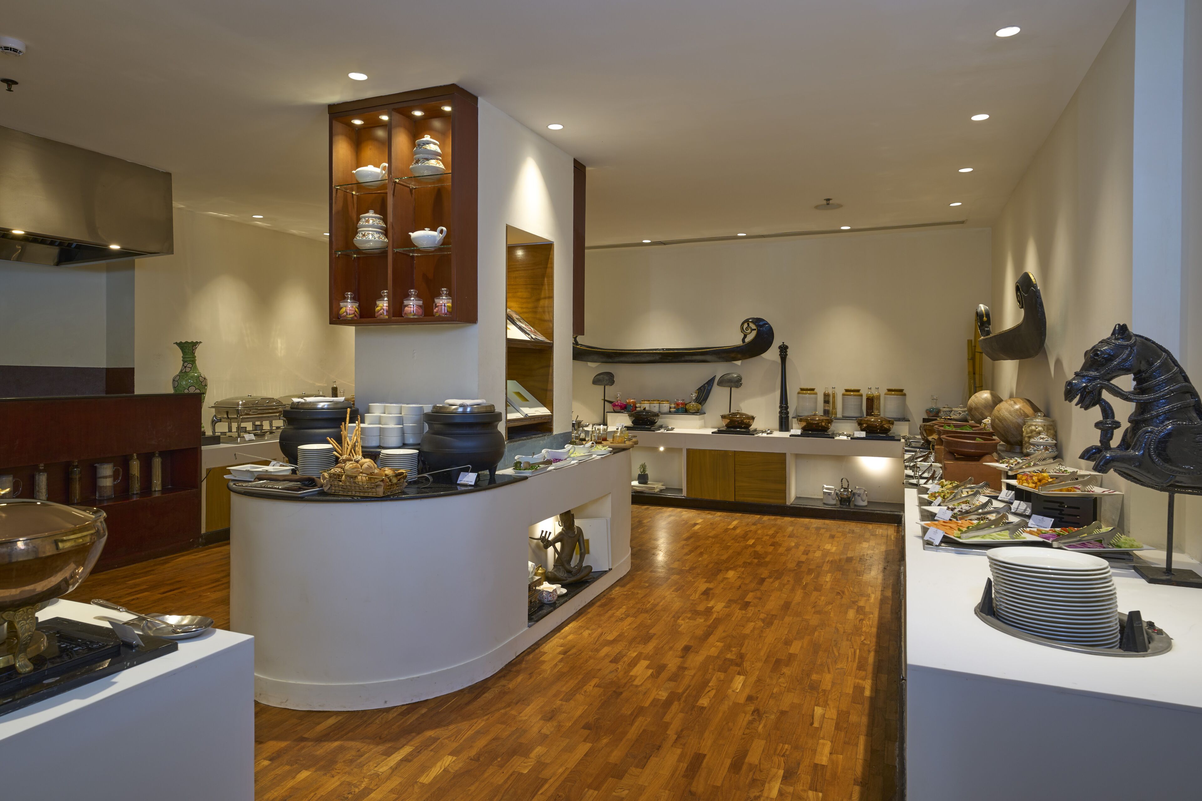A modern kitchen with wooden flooring, white countertops, and various kitchenware displayed on shelves and counters.