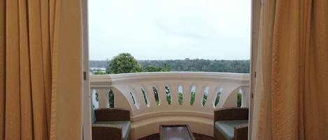 A balcony with a curved railing, wicker furniture, and a view of a forested landscape.