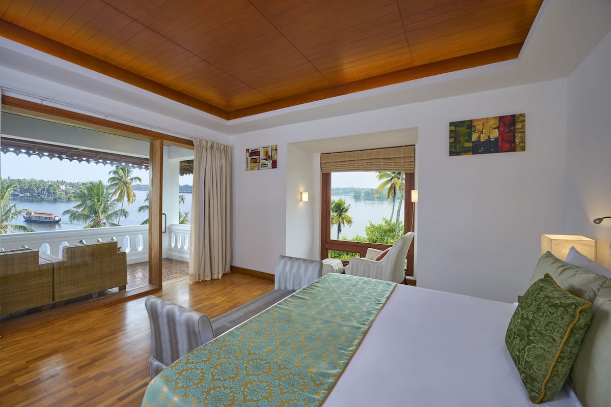A hotel room with a large bed, a balcony with a view of the sea, and a dining area with a table and chairs.