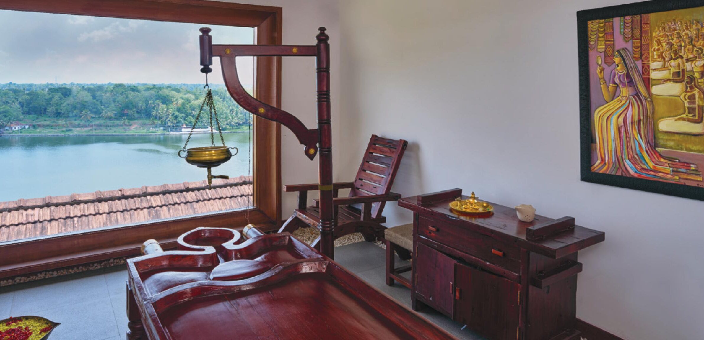 A traditional room with a wooden bed, a brass oil lamp, and a view of a lake.