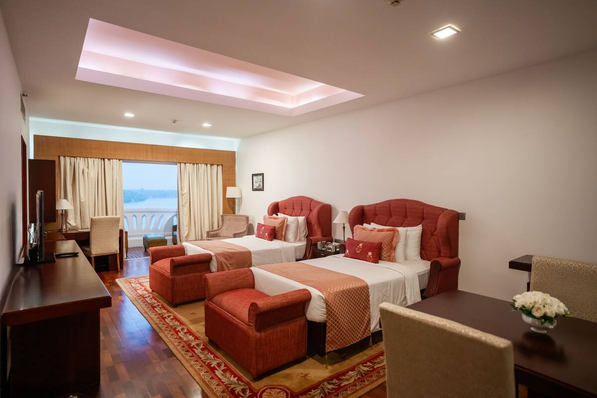 A hotel room with two beds, a desk, a chair, and a view of the city.