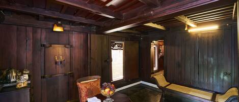 A wooden-paneled room with a bench, a small table with a fruit bowl, and a lamp.