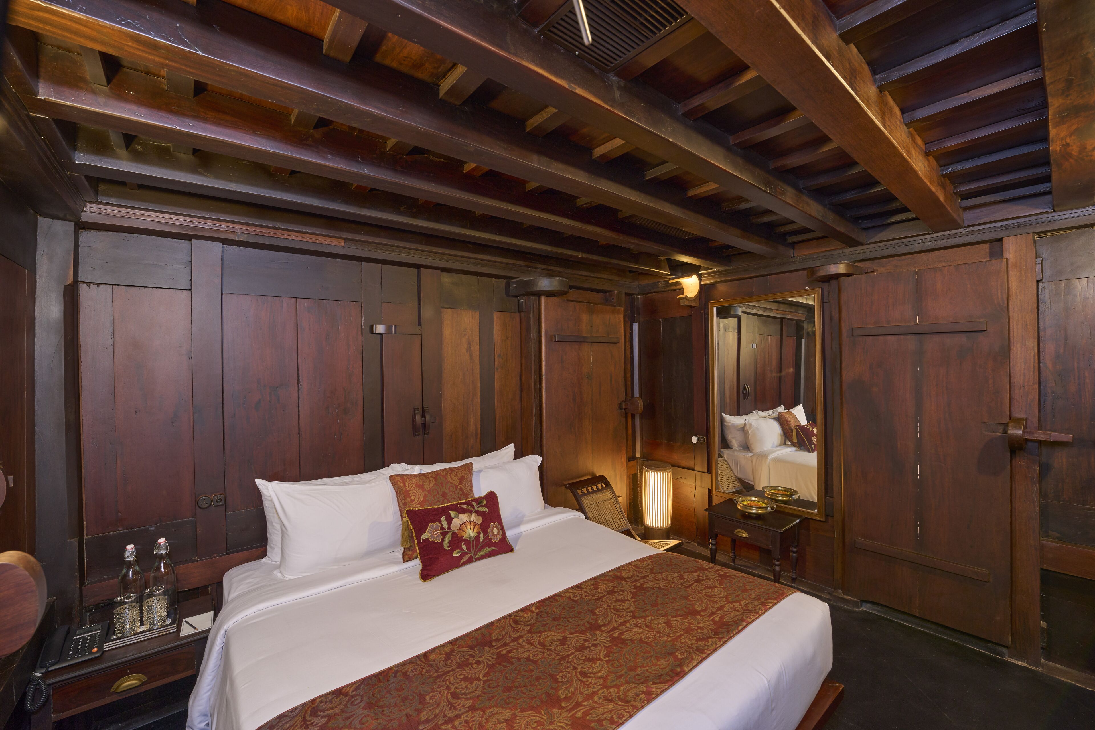 Habitación con paneles de madera, una cama grande, una mesita de noche y un espejo, además de techo de madera.