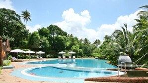 A swimming pool with lounge chairs and umbrellas, surrounded by lush greenery and palm trees.