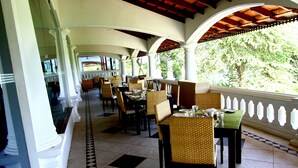 A covered outdoor dining area with white columns, wicker chairs, and tables set for dining.