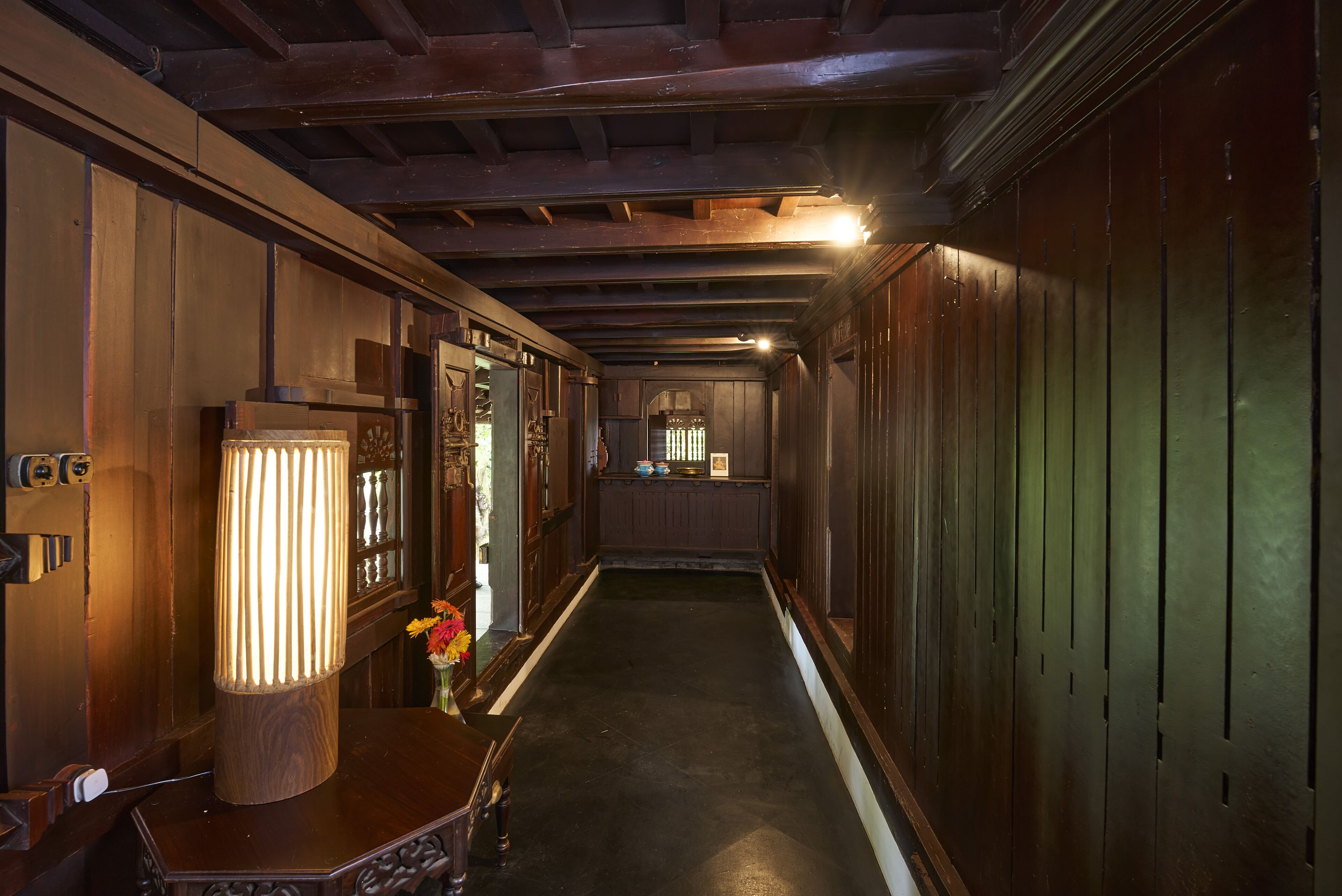 A narrow hallway with wooden paneling, a large floor lamp, and a small table with a vase of flowers.
