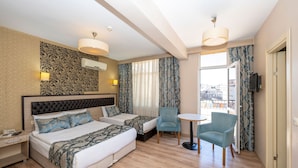 A hotel room with two beds, a small table, two chairs, a TV, and a balcony with curtains. - Tugra Hotel (Istanbul)
