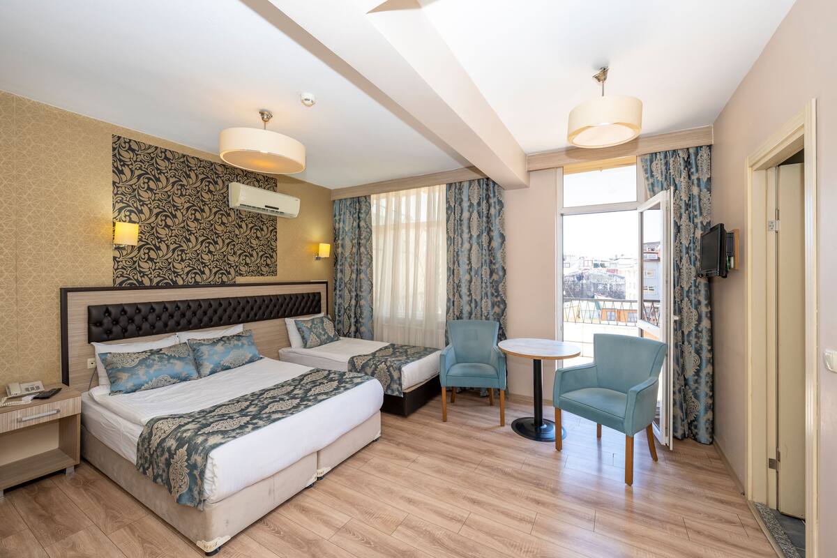 Une chambre d’hôtel avec deux lits, une petite table, deux chaises, un téléviseur et un balcon avec des rideaux.