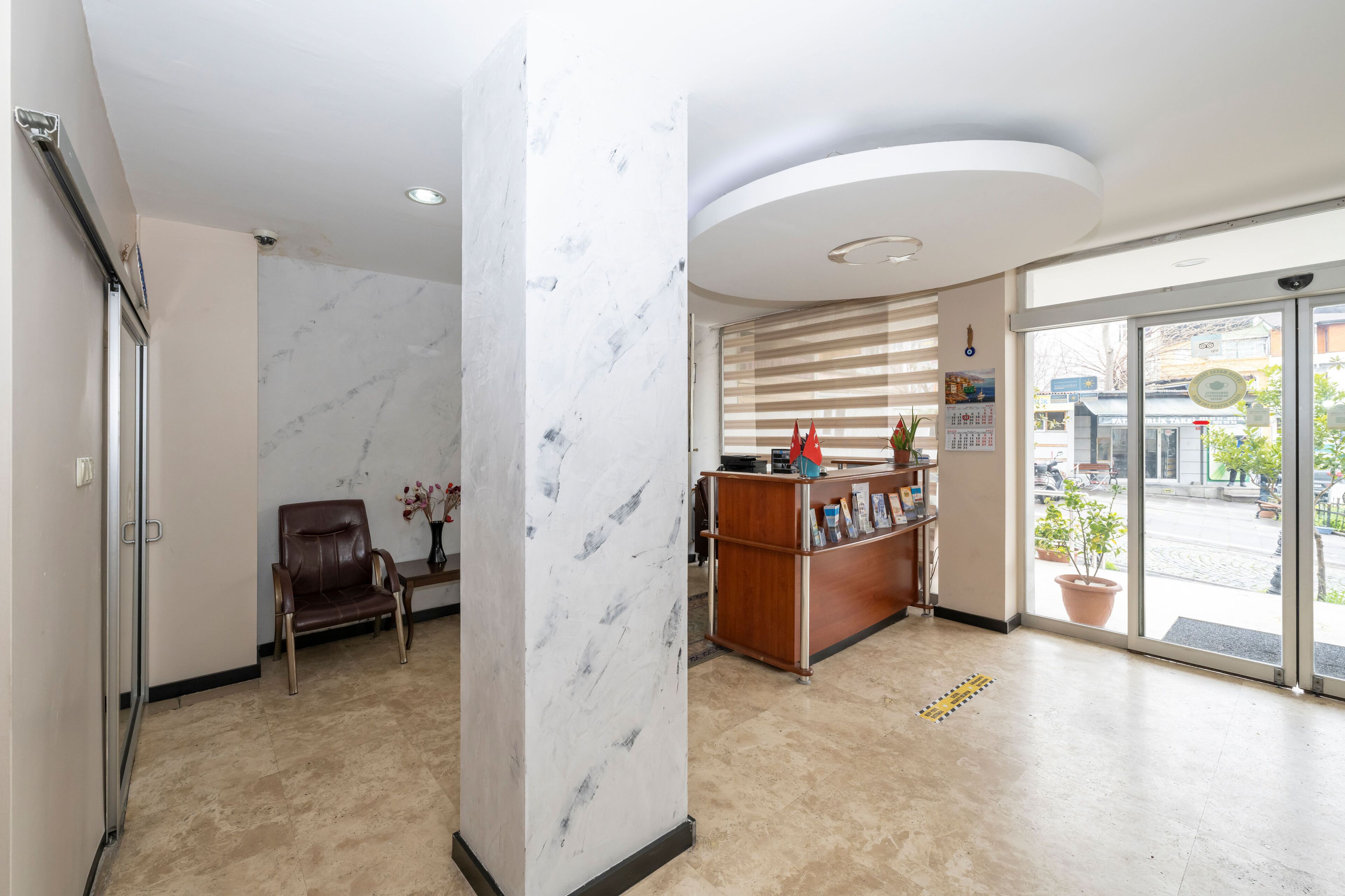 Un área de recepción con una columna de mármol, un mostrador de recepción, un sillón de cuero marrón y vistas a la calle a través de puertas de vidrio.