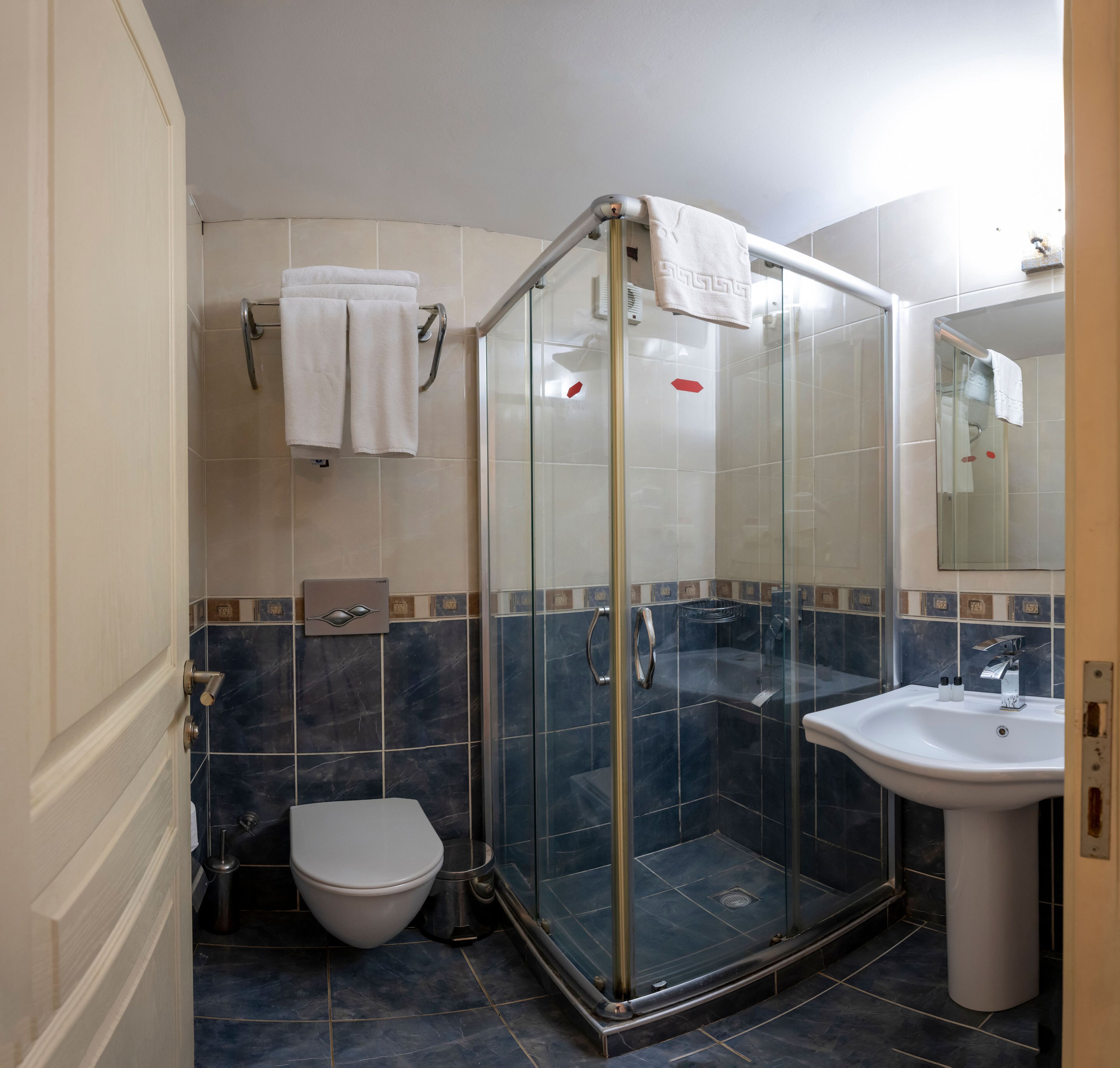 Un baño con ducha compartimentada por vidrio, un lavamanos blanco y un inodoro.